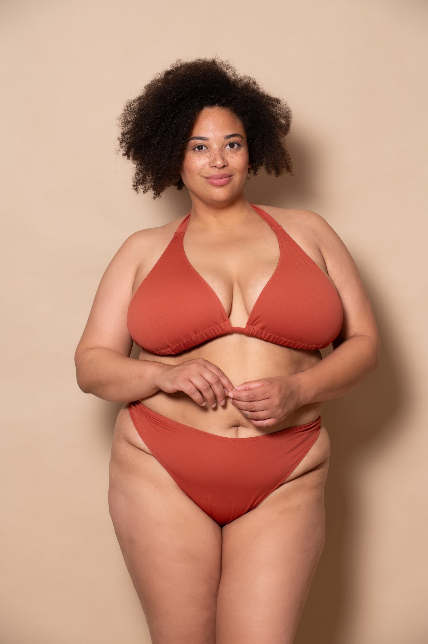 plussize woman wearing a rust red bikini against a beige background