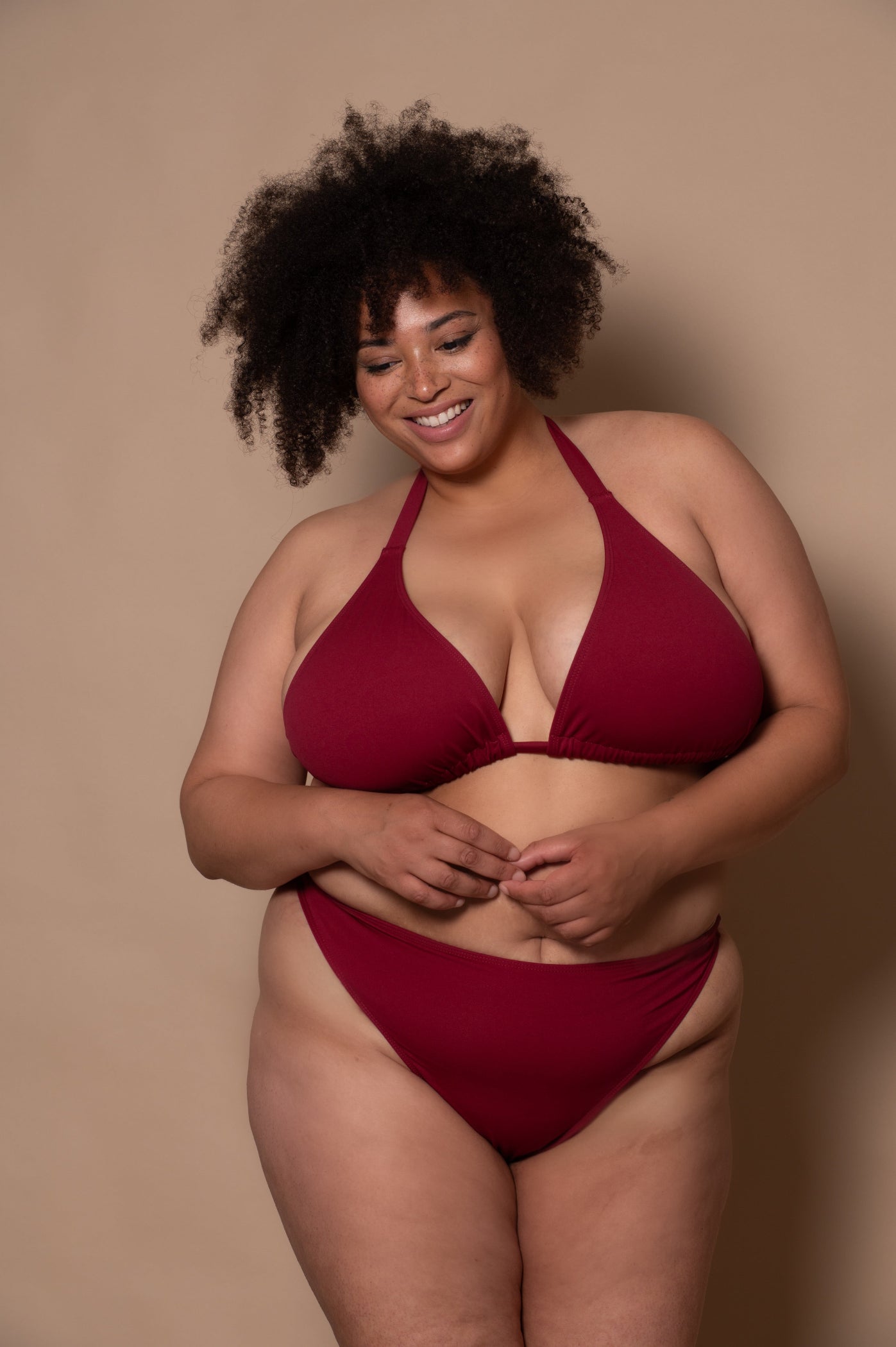 plussize woman wearing a wine red bikini against a beige background