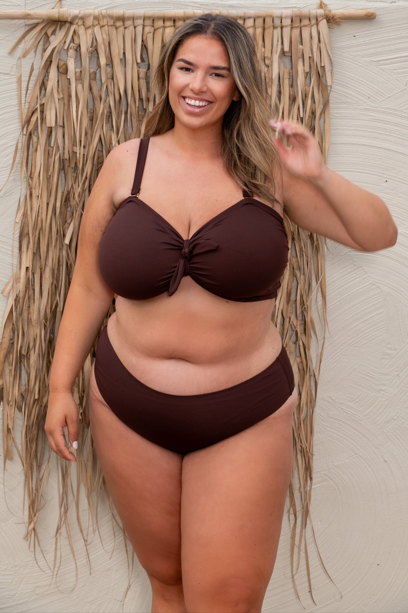 plussize woman wearing a chocolate brown bikini against a beige background