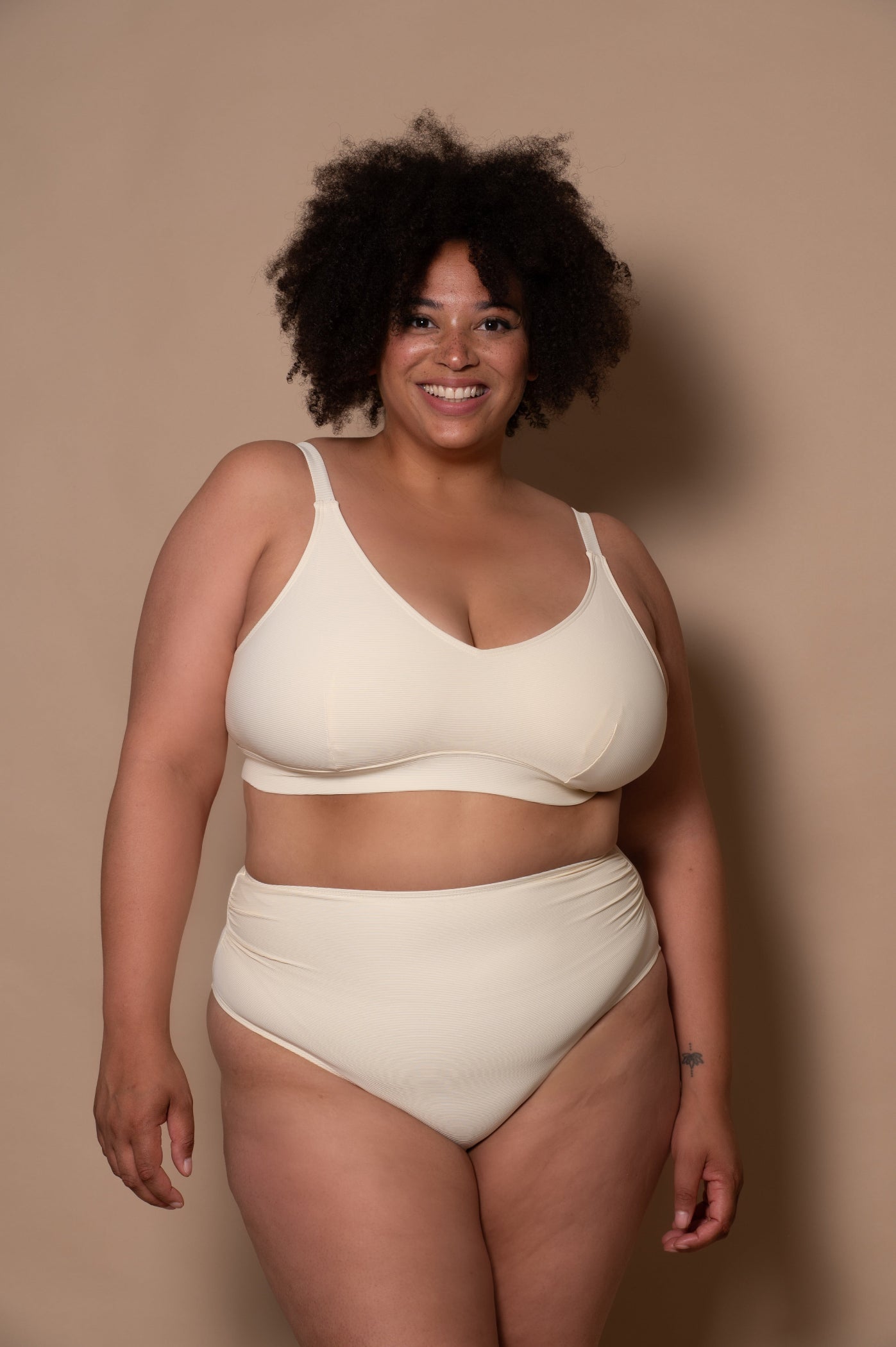 curvy woman wearing a cream - white bikini against a beige background