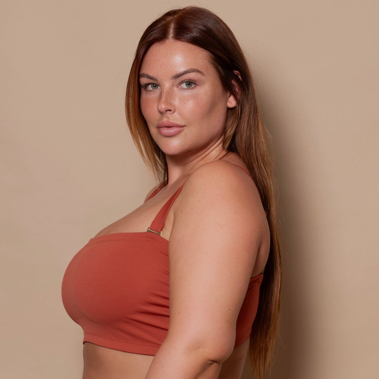 plussize woman wearing a rust red bikini set against a beige background