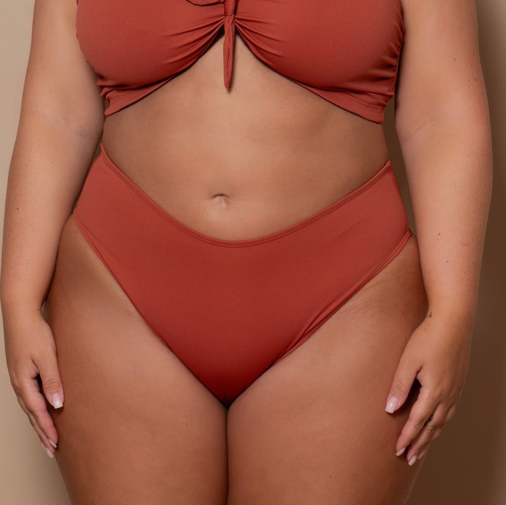 plussize woman wearing a rust red bikini set against a beige background
