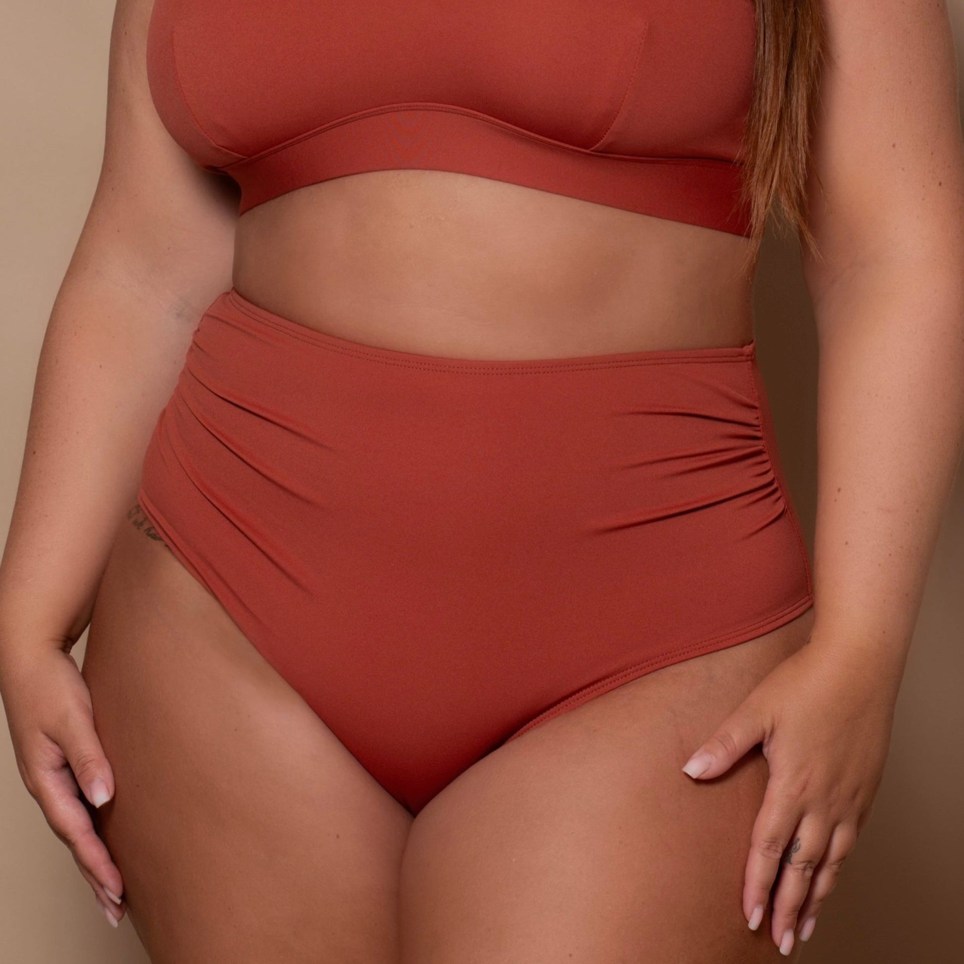 plussize woman wearing a rust red bikini set against a beige background