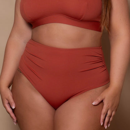 plussize woman wearing a rust red bikini set against a beige background