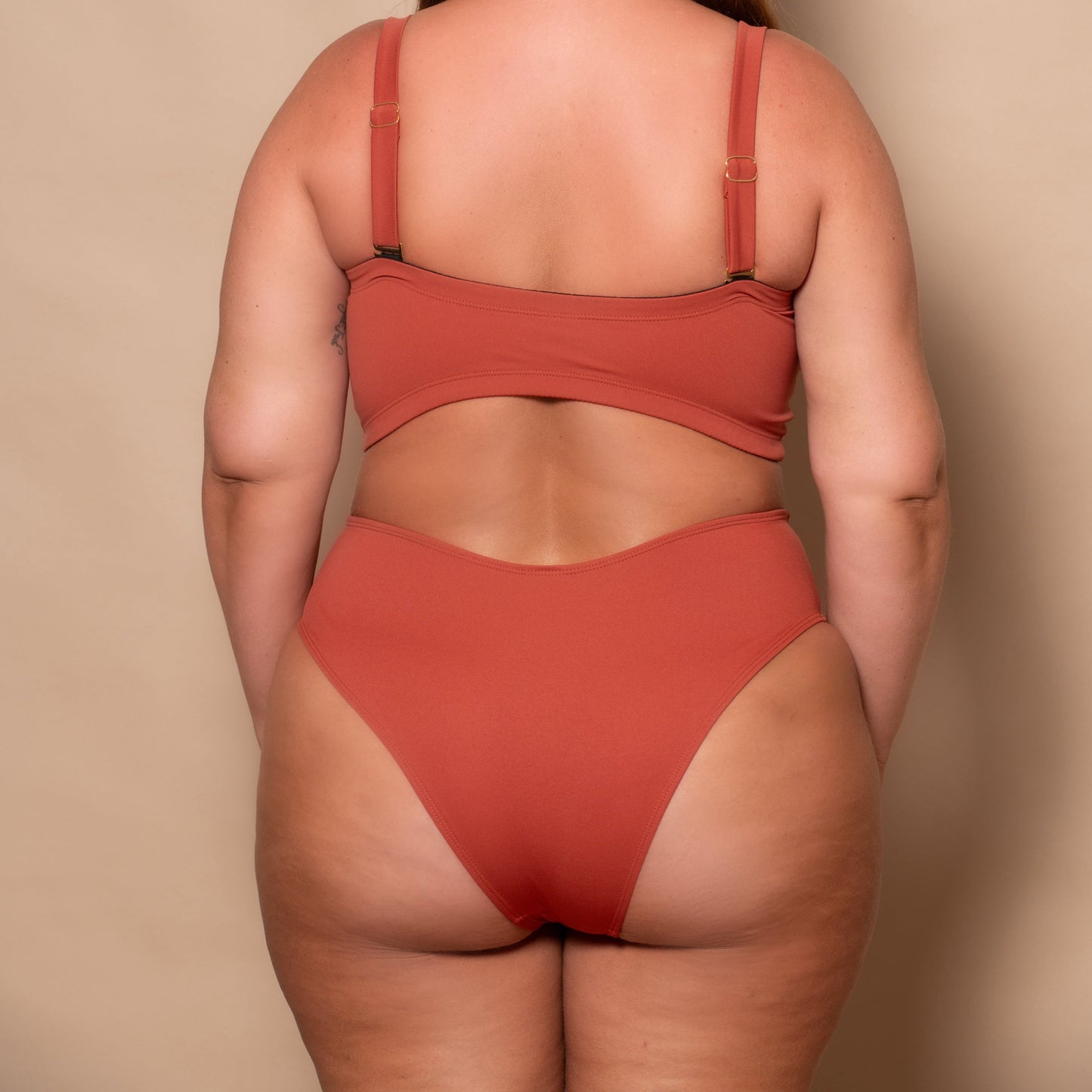 plussize woman wearing a rust red bikini set against a beige background