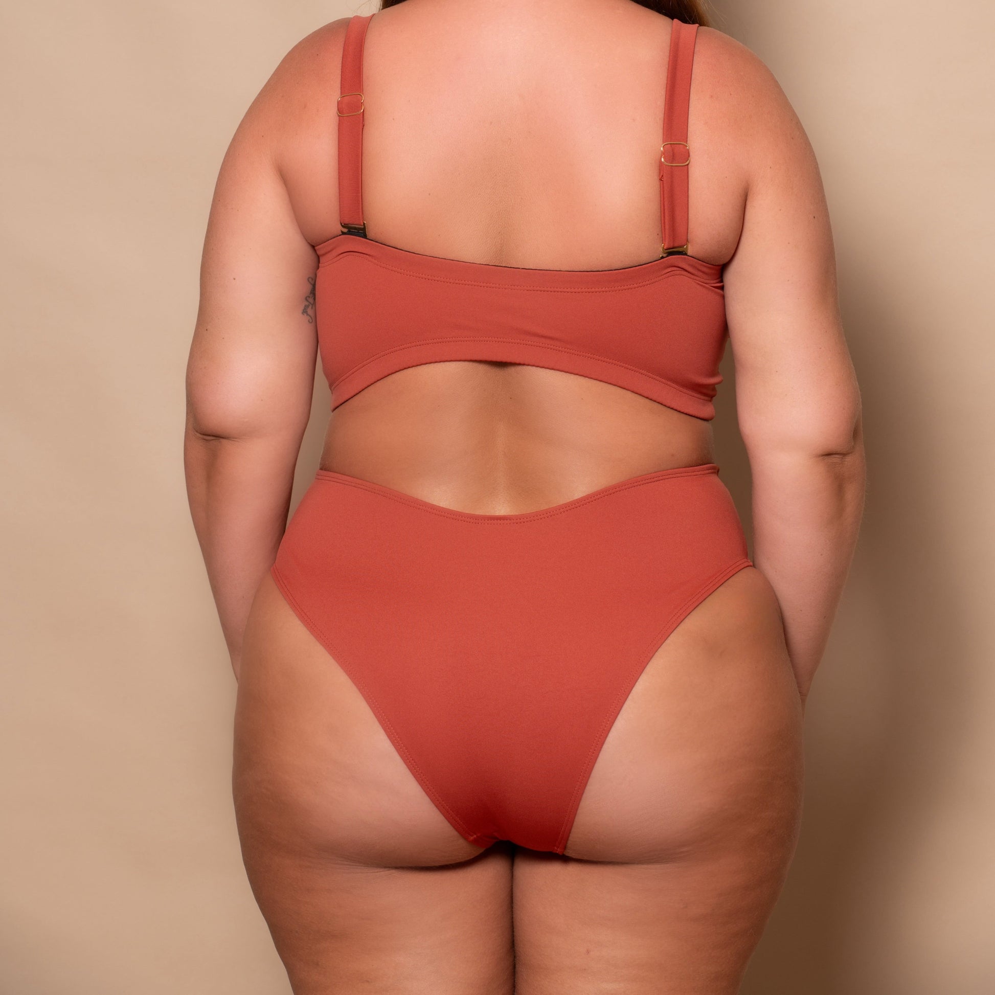plussize woman wearing a rust red bikini set against a beige background