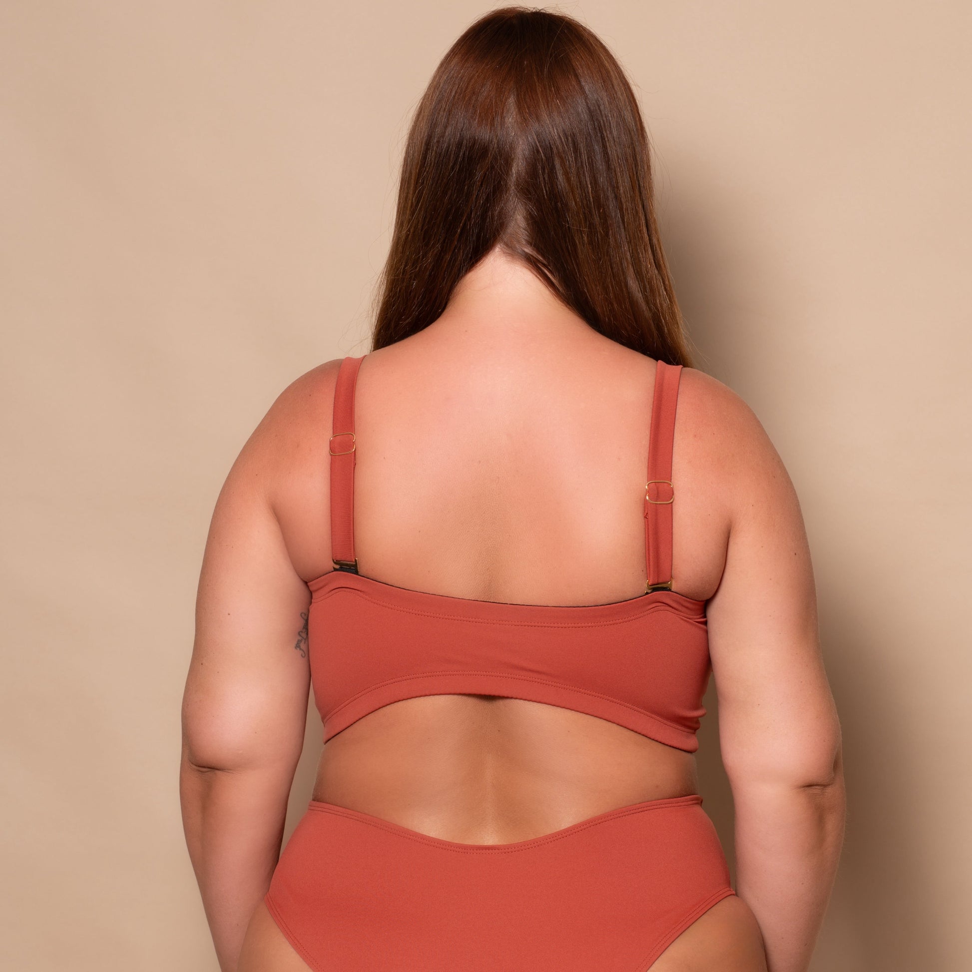 plussize woman wearing a rust red bikini set against a beige background