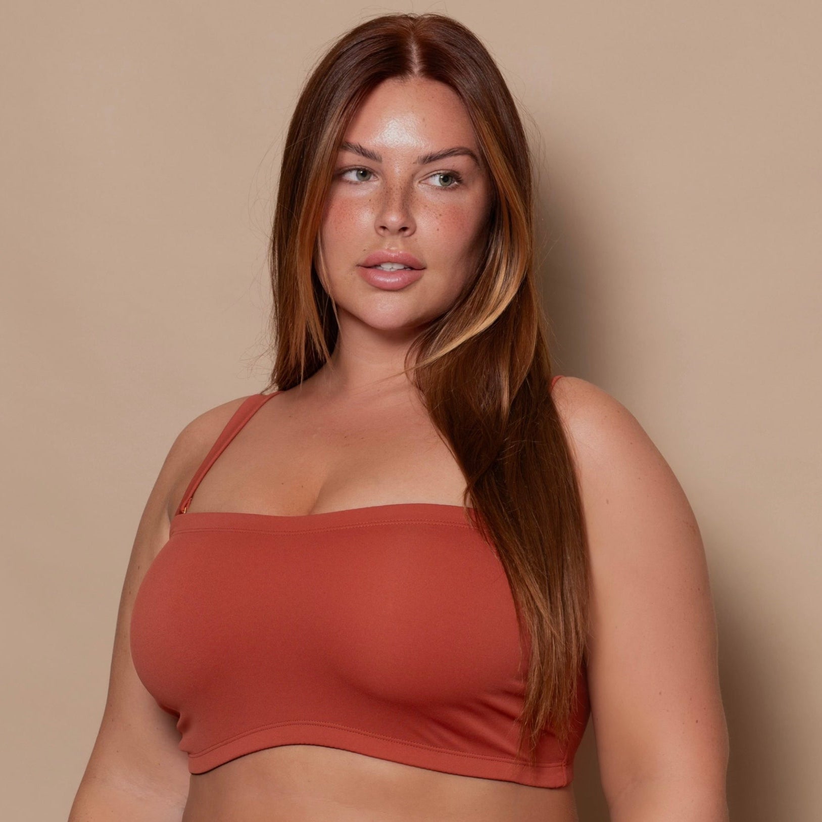 plussize woman wearing a rust red bikini set against a beige background