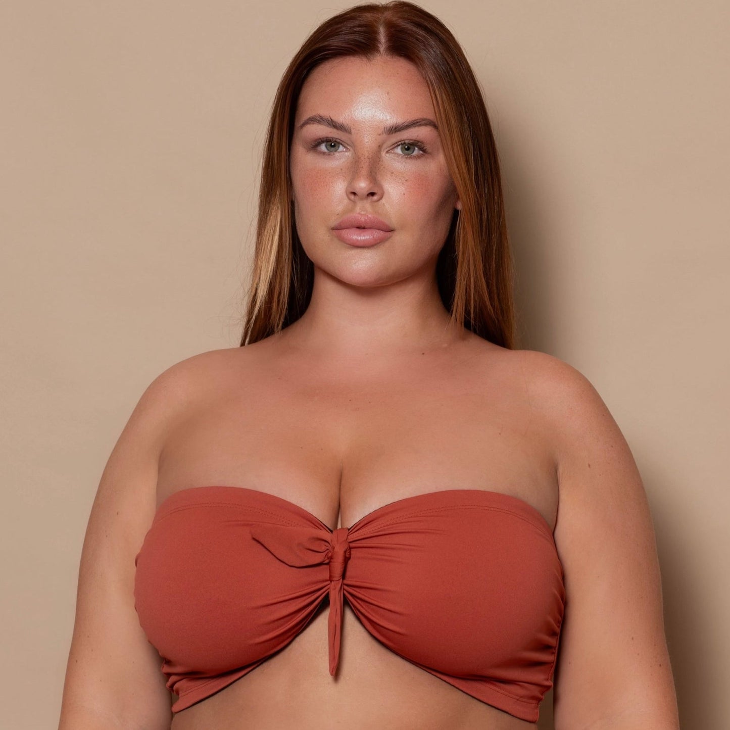 plussize woman wearing a rust red bikini set against a beige background