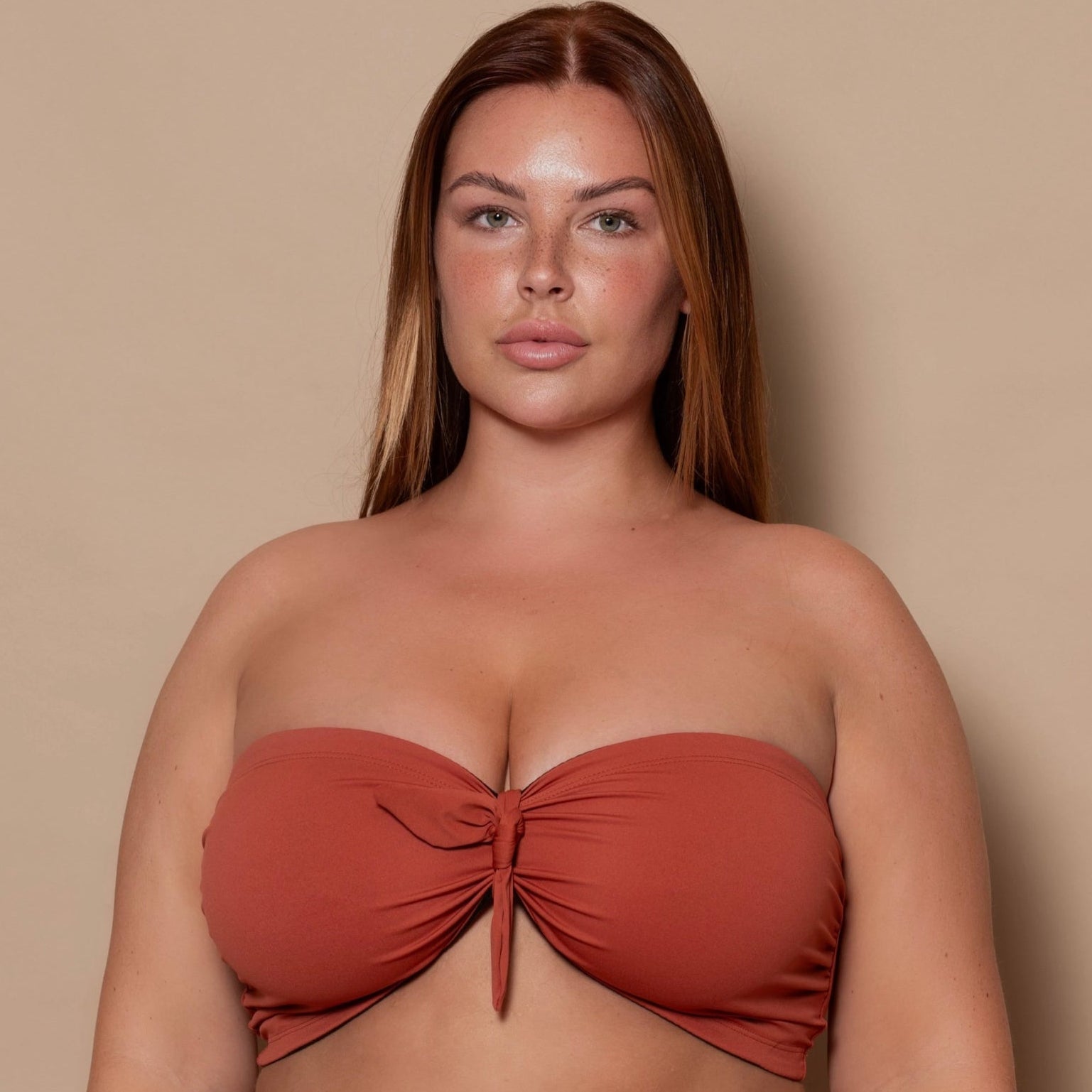 plussize woman wearing a rust red bikini set against a beige background