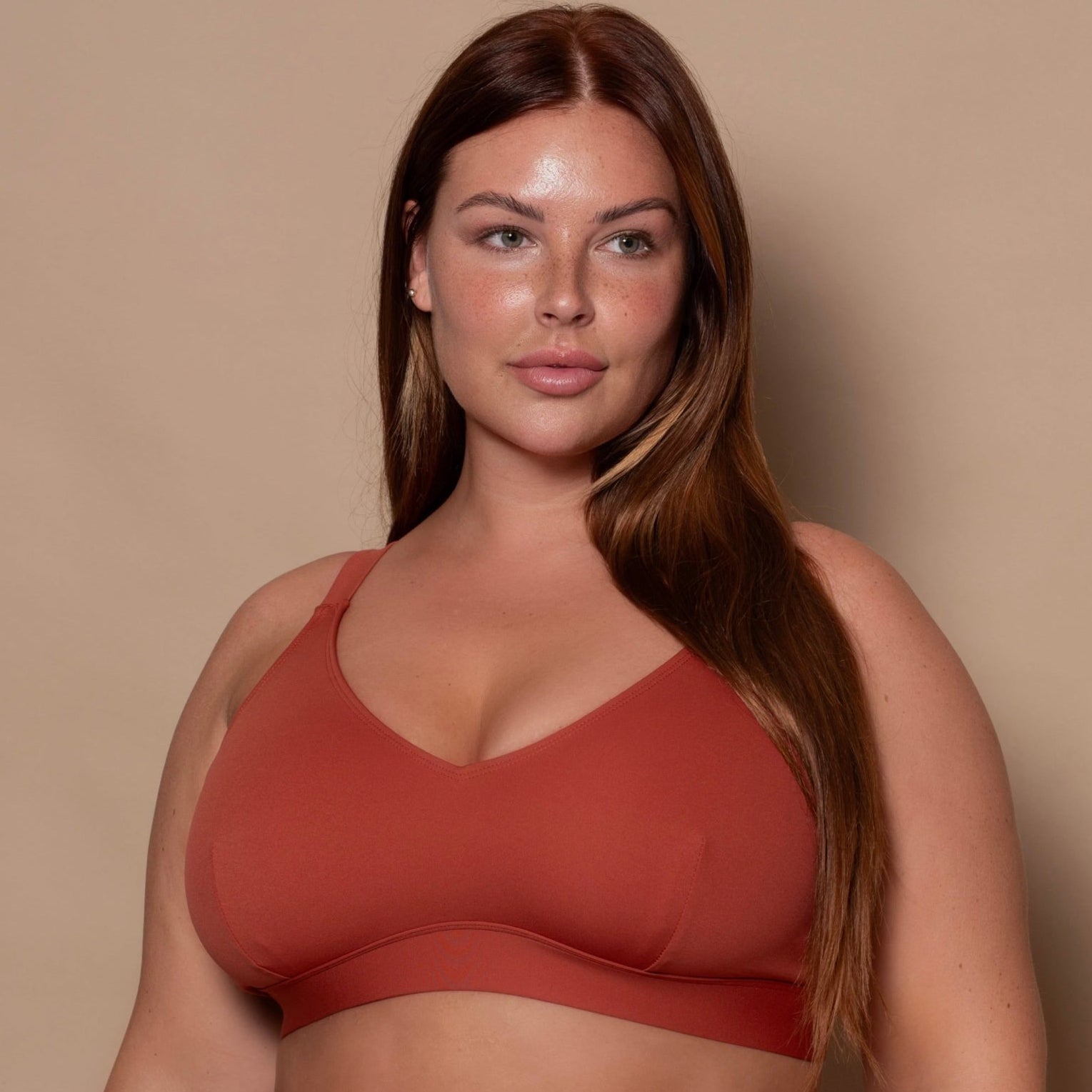 plussize woman wearing a rust red bikini set against a beige background