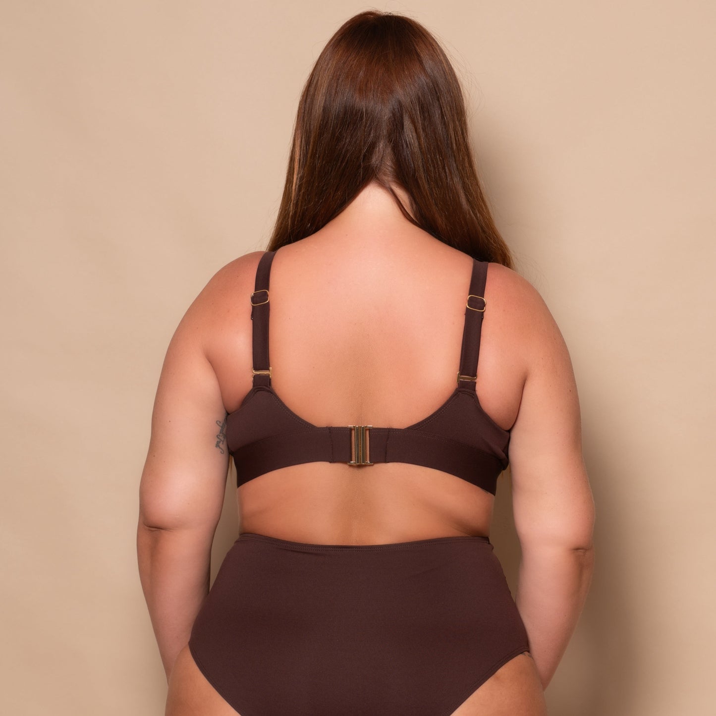 plussize woman wearing a chocolate brown bikini set against a beige background
