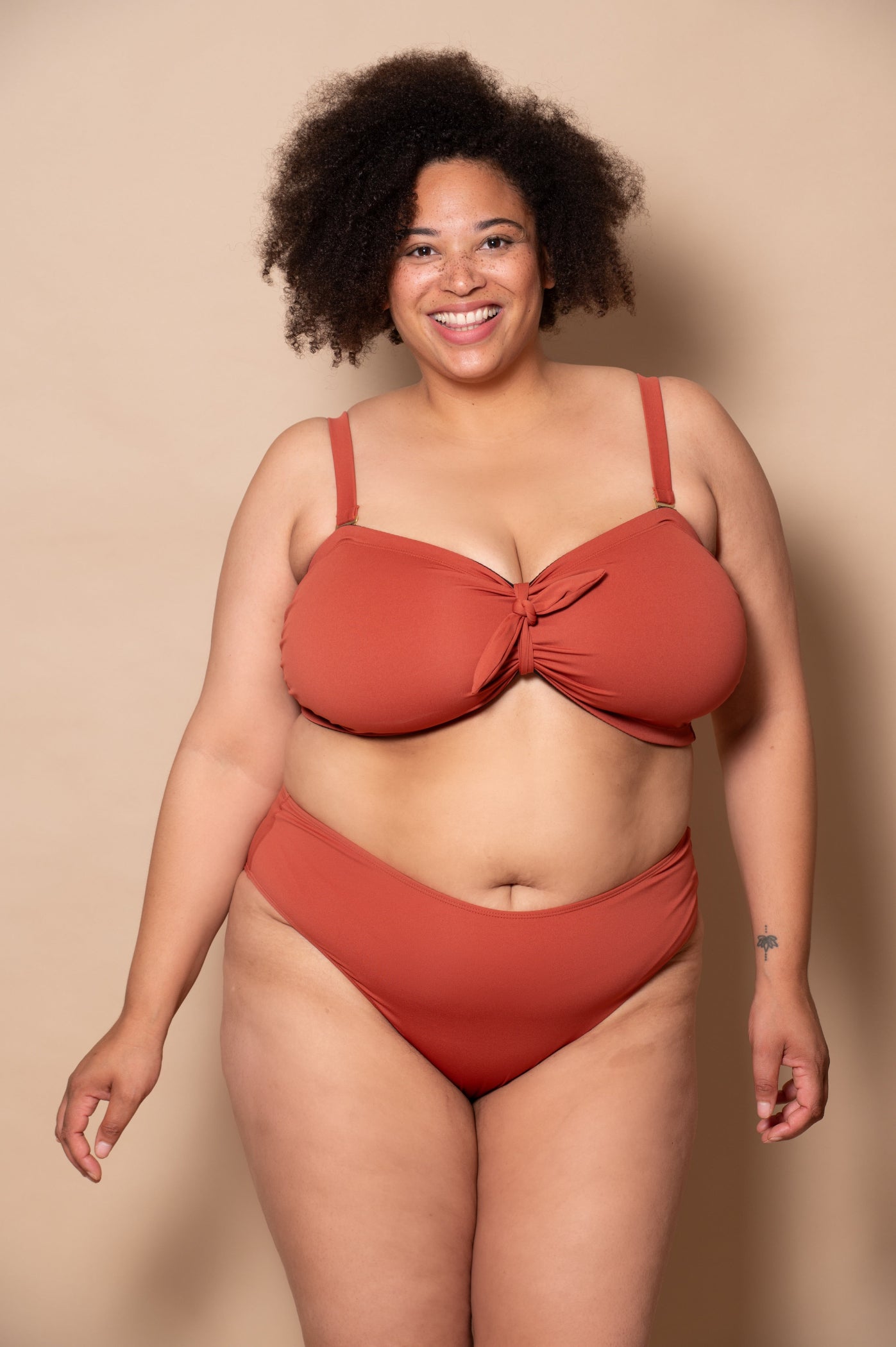 plussize woman wearing a rust red bikini  against a beige background