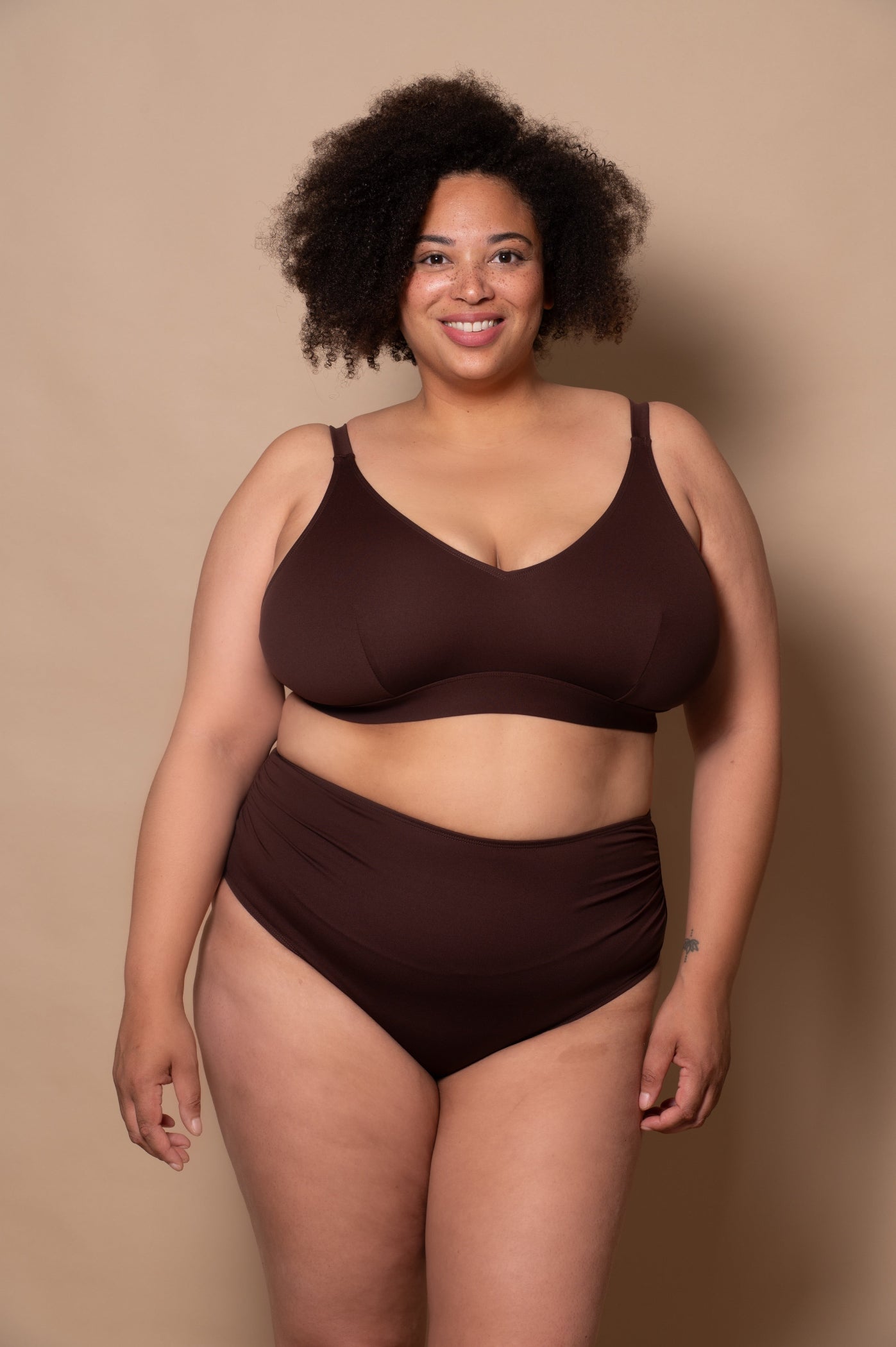 plussize woman wearing a chocolate brown bikini  against a beige background