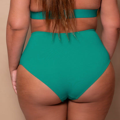 curvy Woman in an emerald green bikini standing in front of a beige background