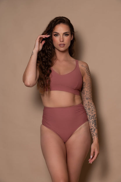 Woman wearing a rosewood - pink bikini against a beige background