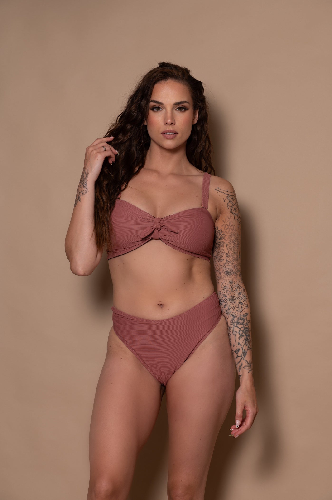 woman wearing a pink rosewood bikini standing against a textured wall.
