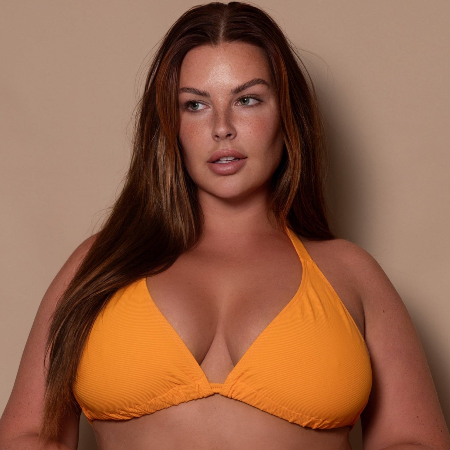 curvy woman wearing a yellow ribbed bikini triangle against a beige background