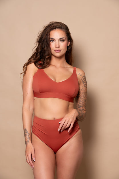 Woman wearing a rust bikini against a beige background