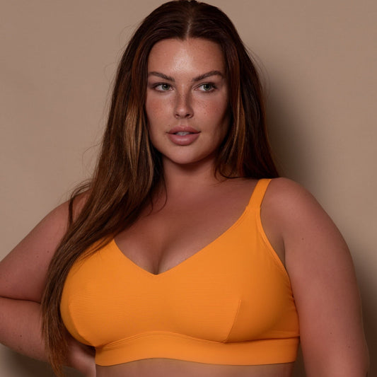curvy woman wearing a yellow ribbed bikini against a beige background