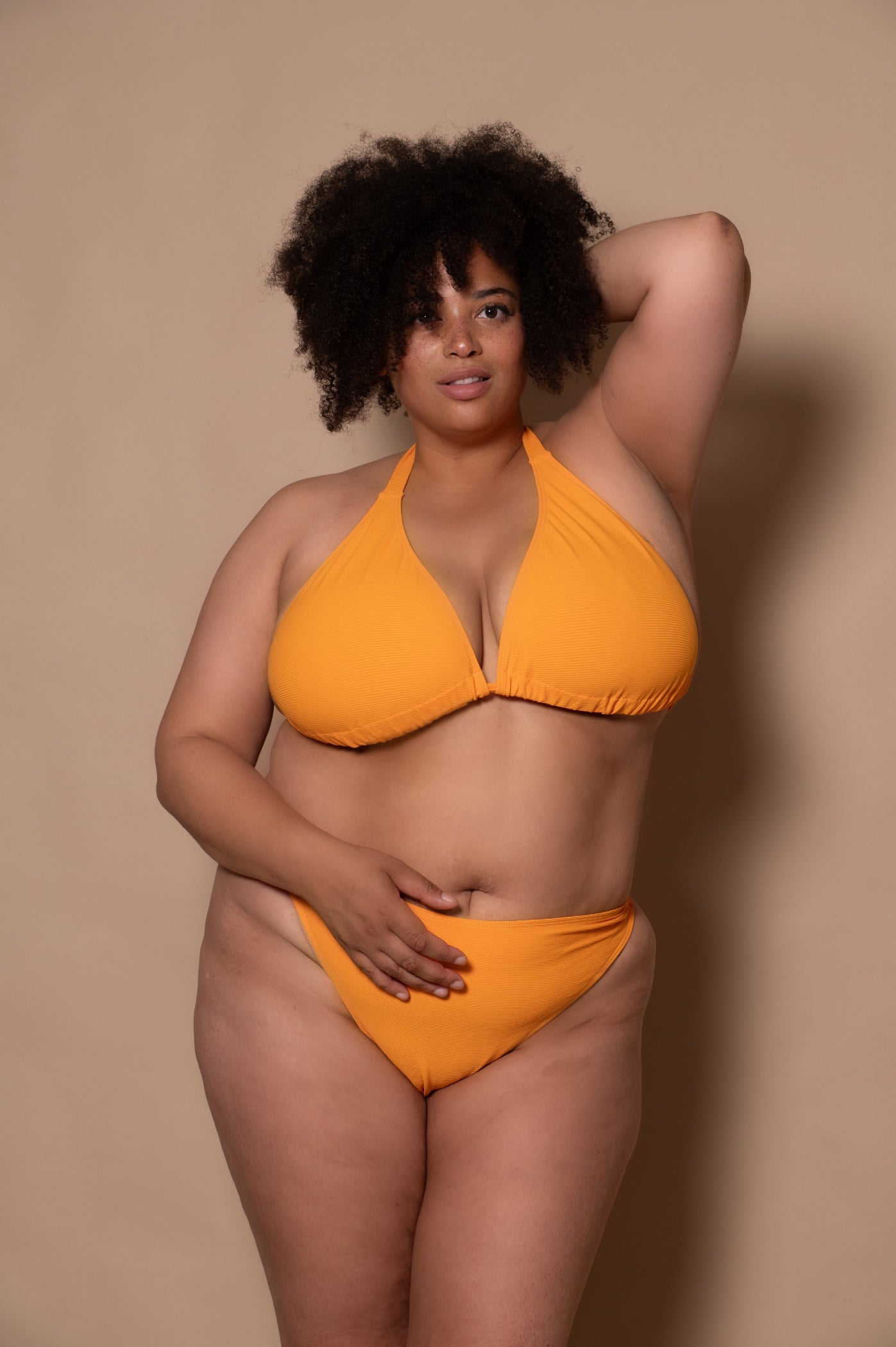 plussize woman wearing a yellow bikini  against a beige background