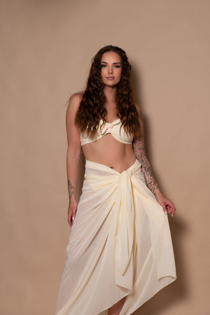 Woman wearing a white cream bikini with pareo cover up against a beige background