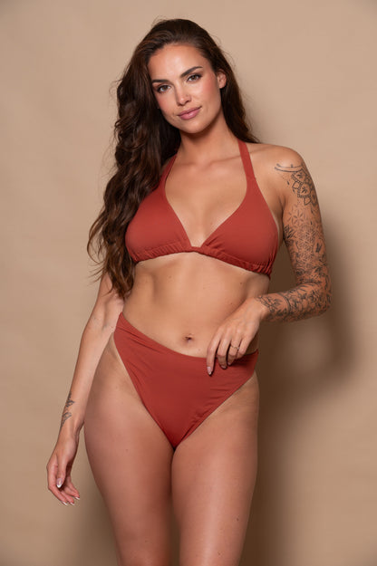 woman wearing a rust red bikini set against a beige background