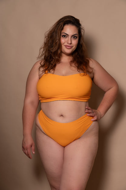 plussize woman wearing a yellow sunflower bikini against a beige background