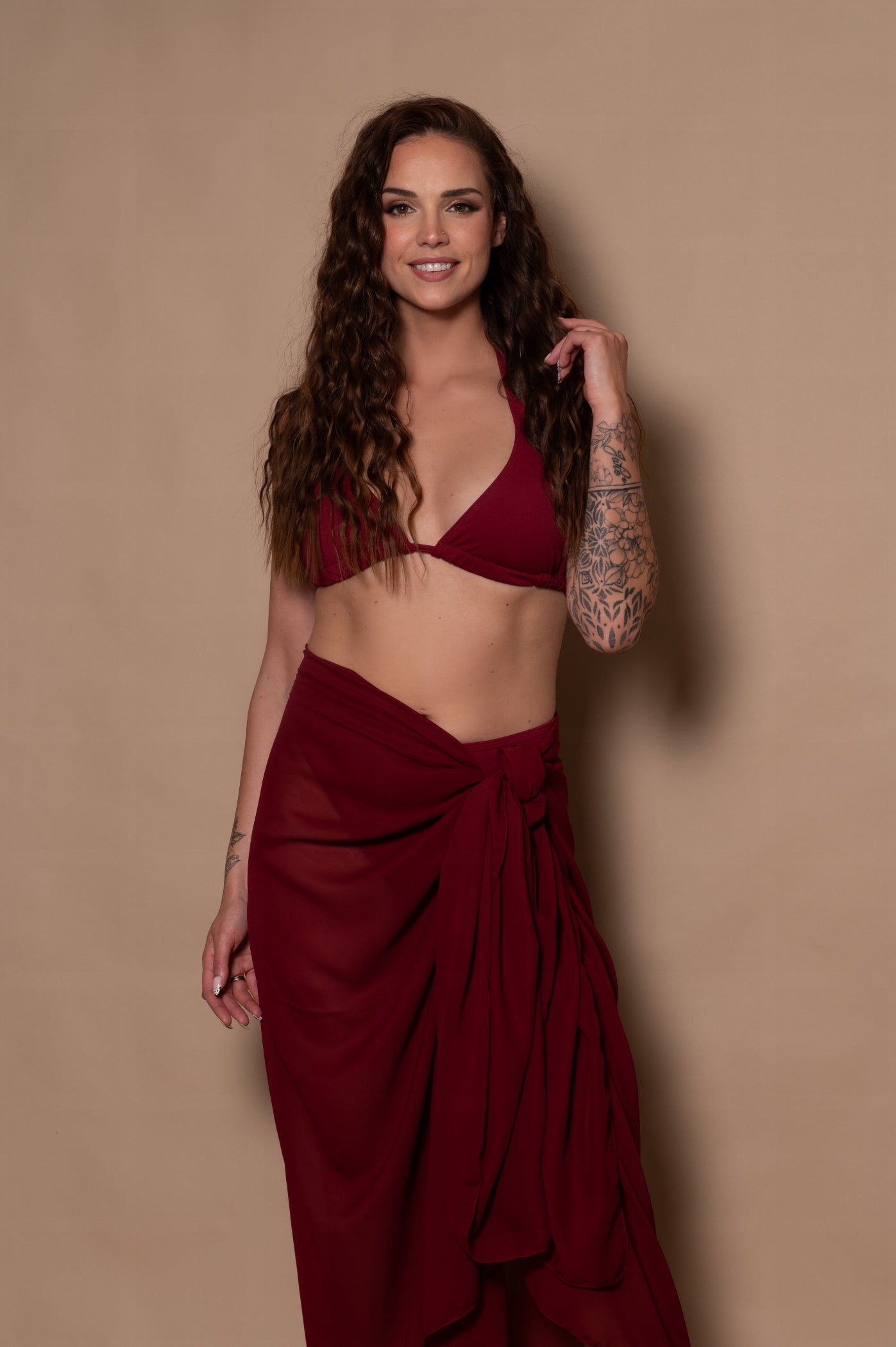 woman wearing a pomegranate red bikini with pareo cover up against a beige background
