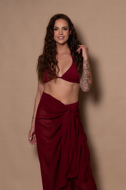 woman wearing a pomegranate red bikini with pareo cover up against a beige background