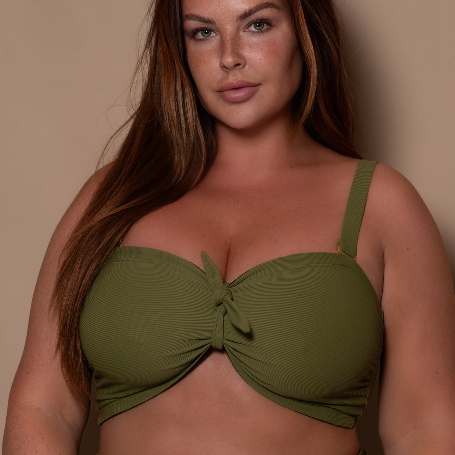 plussize woman wearing a khaki green bandeau bikini  against a beige background
