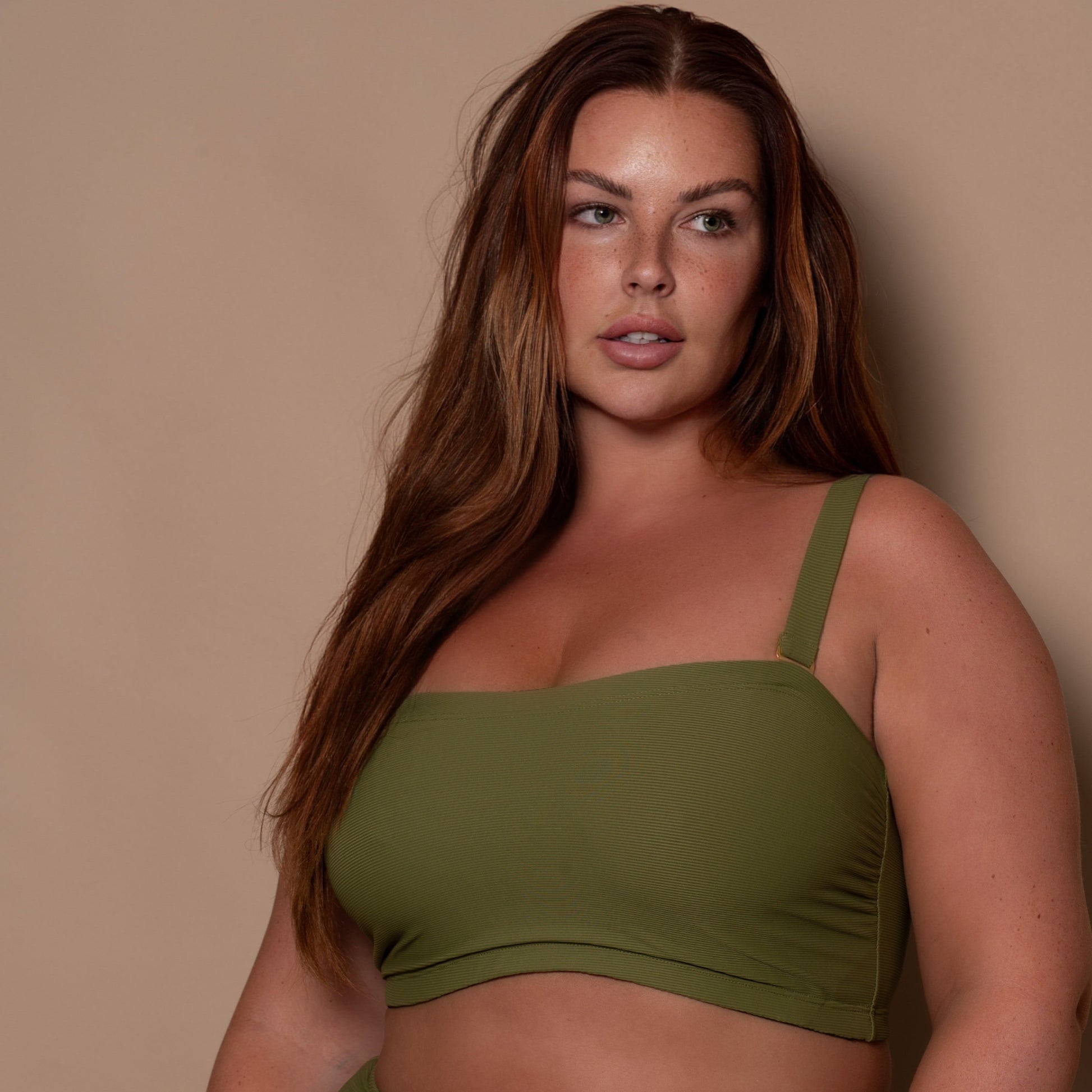 plussize woman wearing a khaki green bandeau bikini  against a beige background