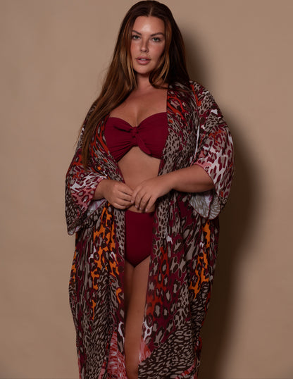Woman wearing a red bikini and patterned kimono cover up against a beige background