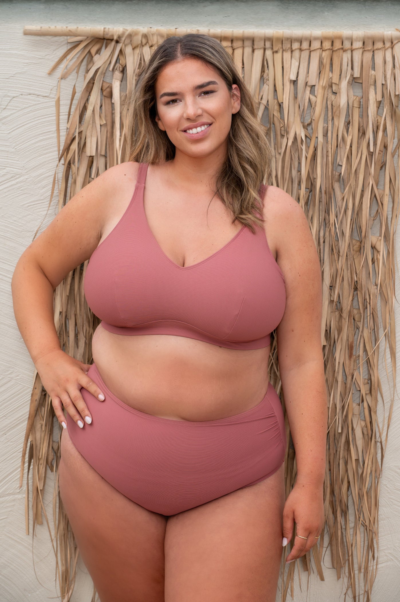 plussize woman wearing a rosewood pink bikini  against a beige background