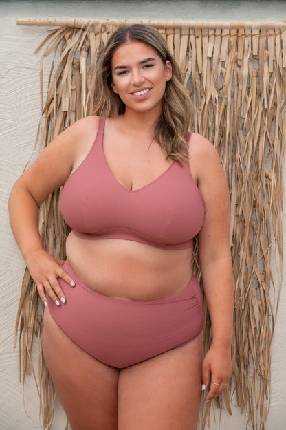 plussize woman wearing a rosewood pink bikini  against a beige background