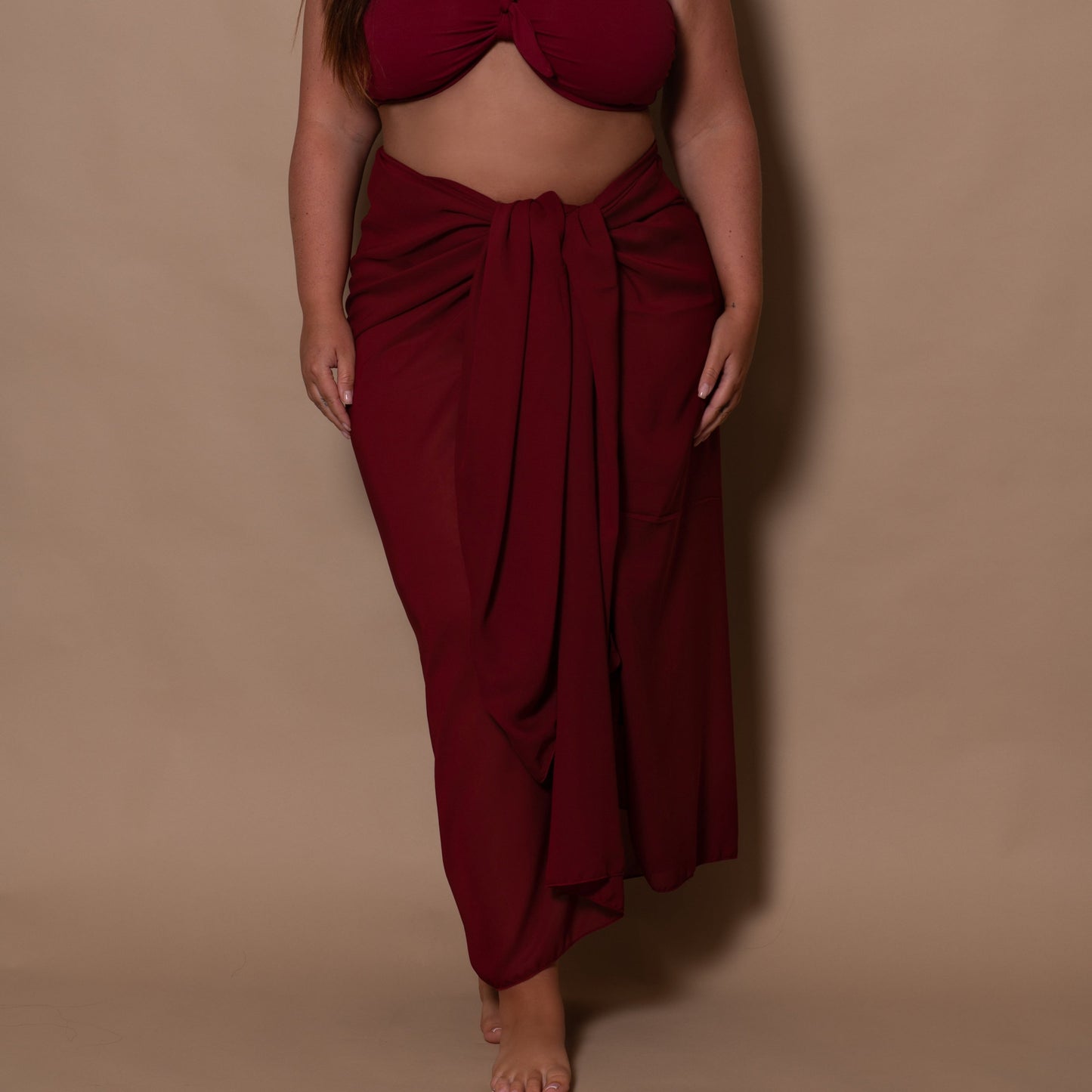 Woman wearing a burgundy strapless top and sarong against a beige background