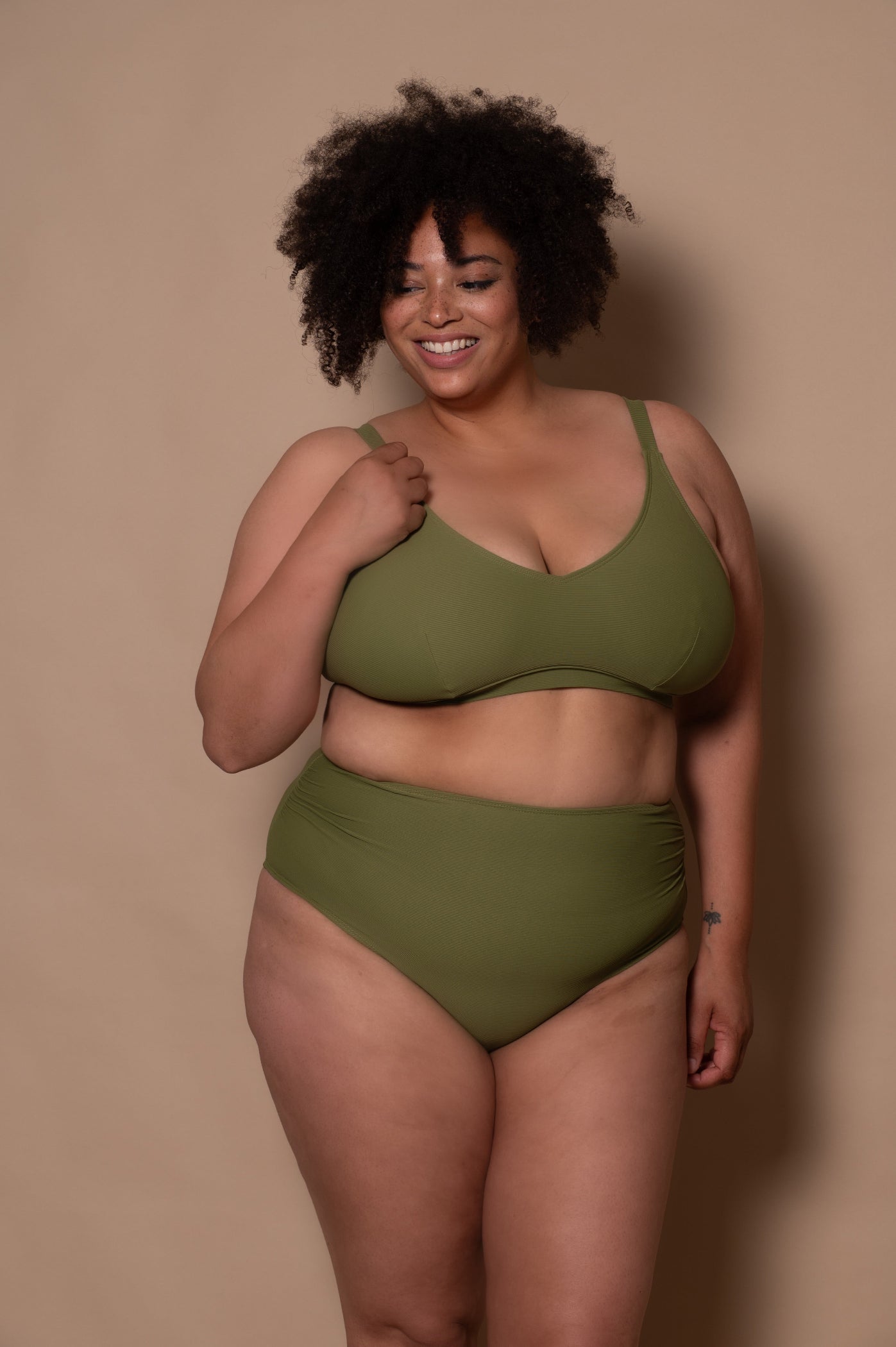 plussize woman wearing a khaki green bikini  against a beige background