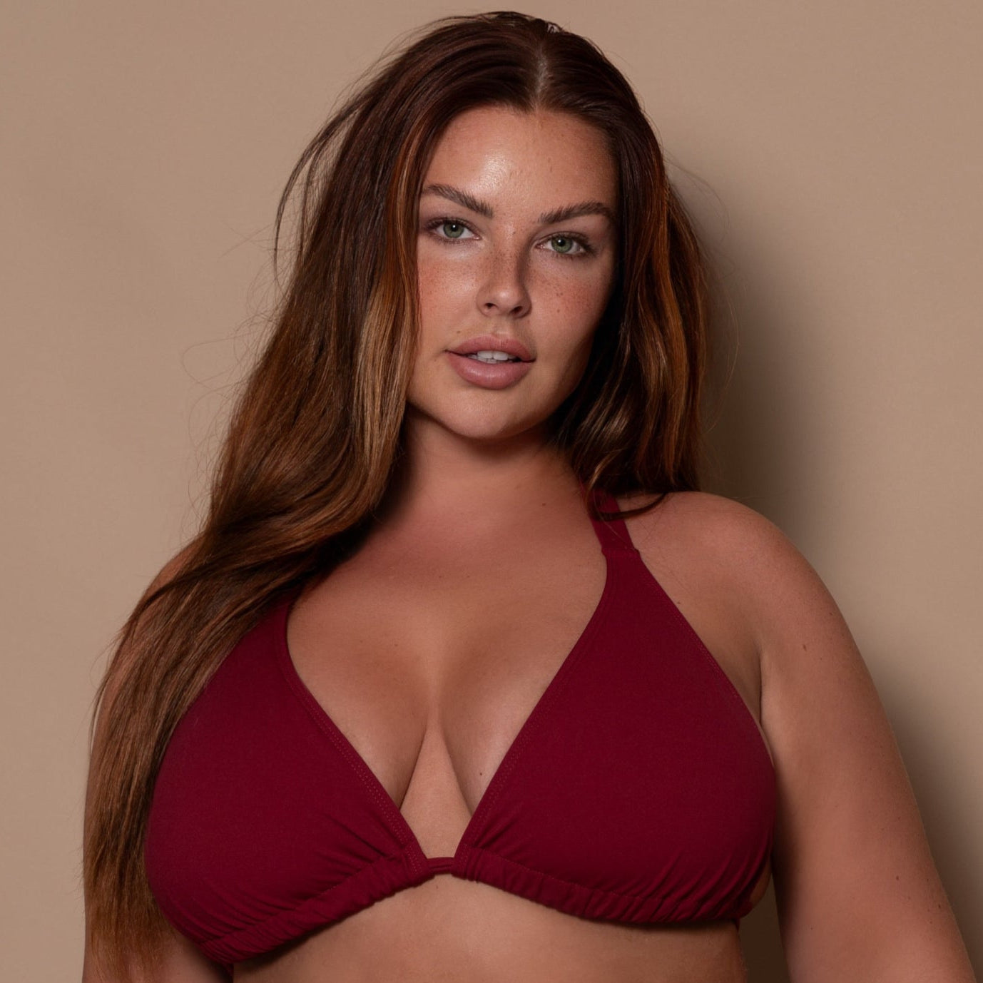 plussize woman wearing a pomegranate red bikini triangle and thong against a beige background