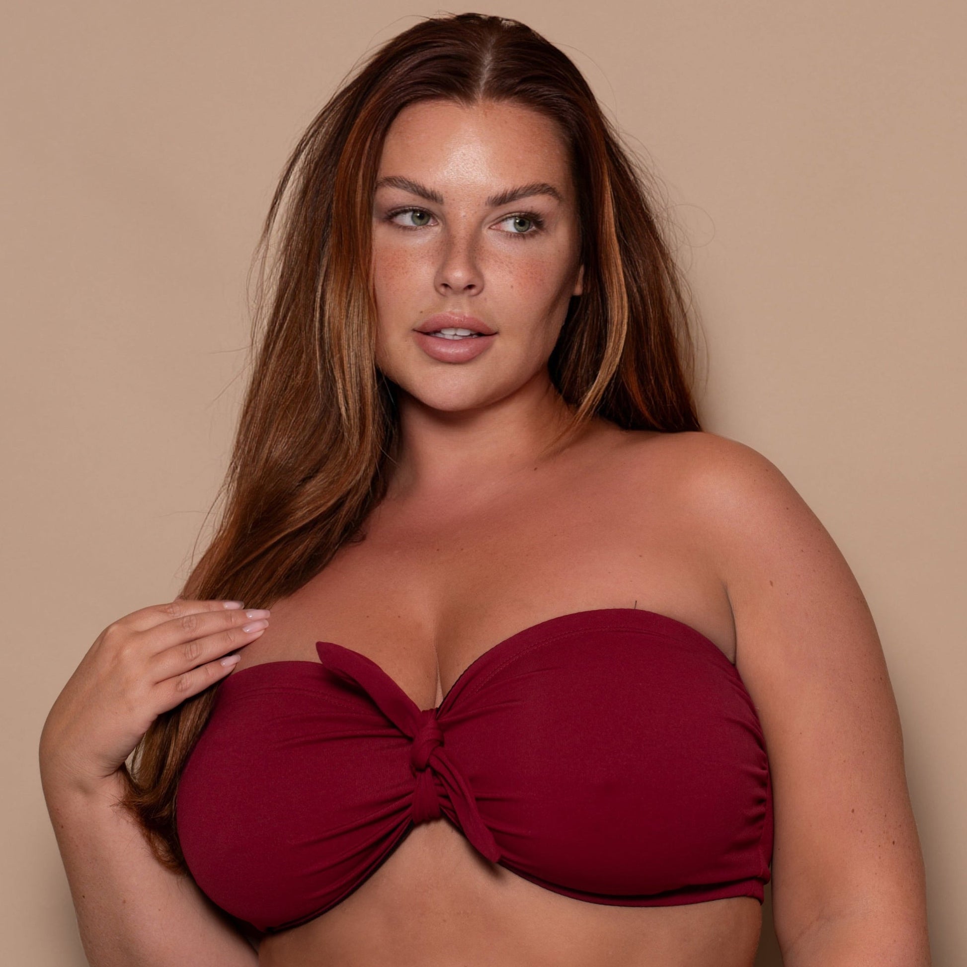 plussize woman wearing a pomegranate red bikini  against a beige background