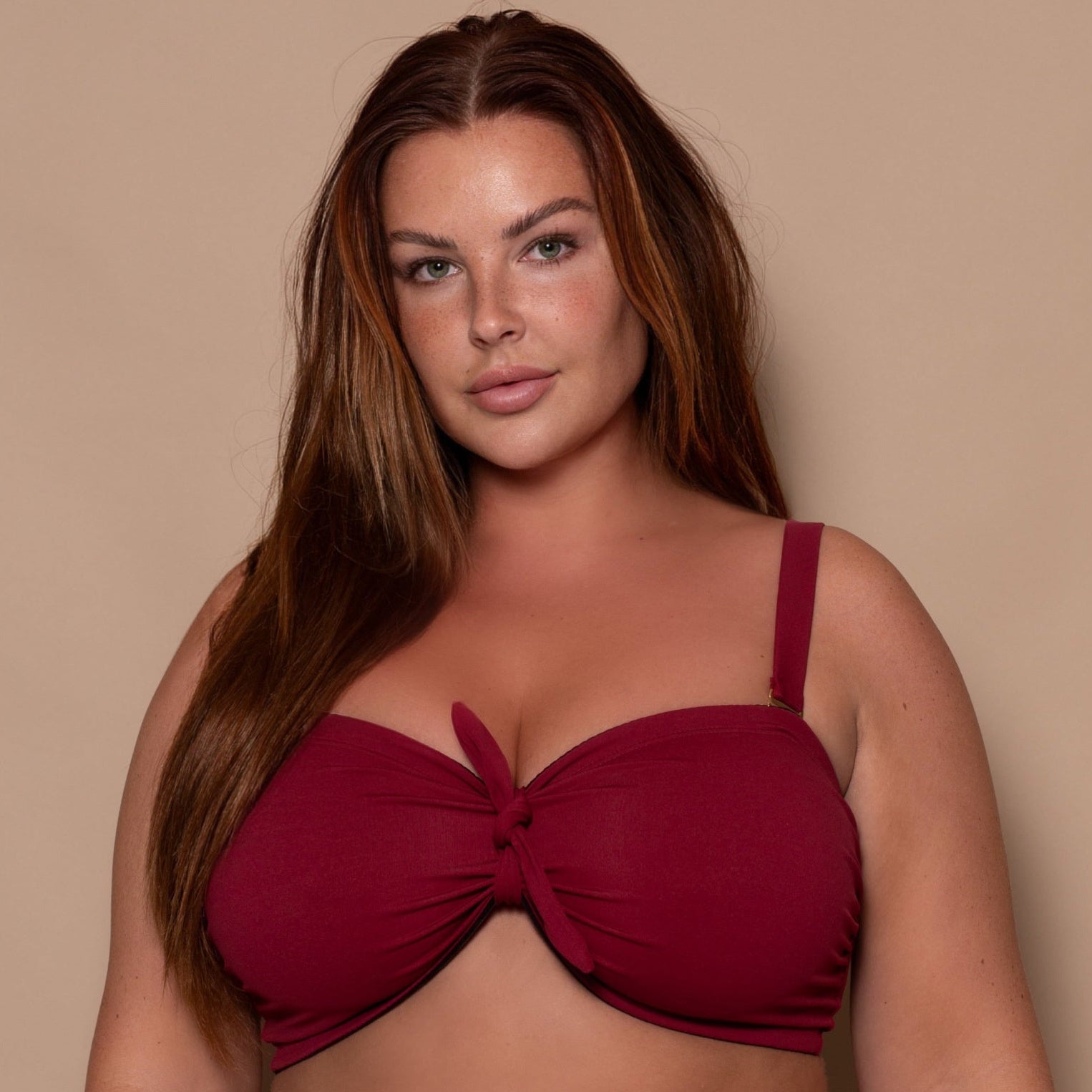 plussize woman wearing a pomegranate red bikini  against a beige background