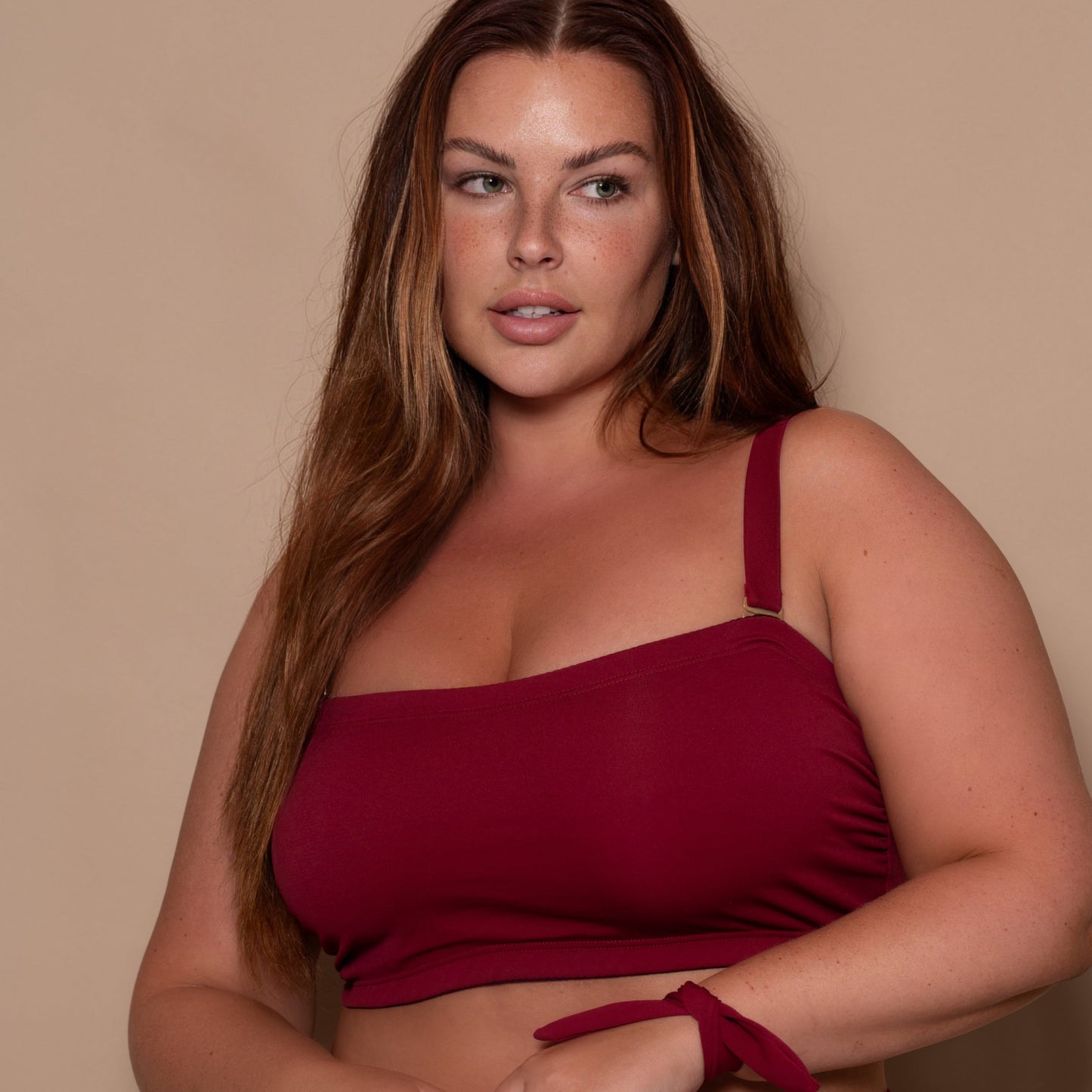 plussize woman wearing a pomegranate red bikini  against a beige background
