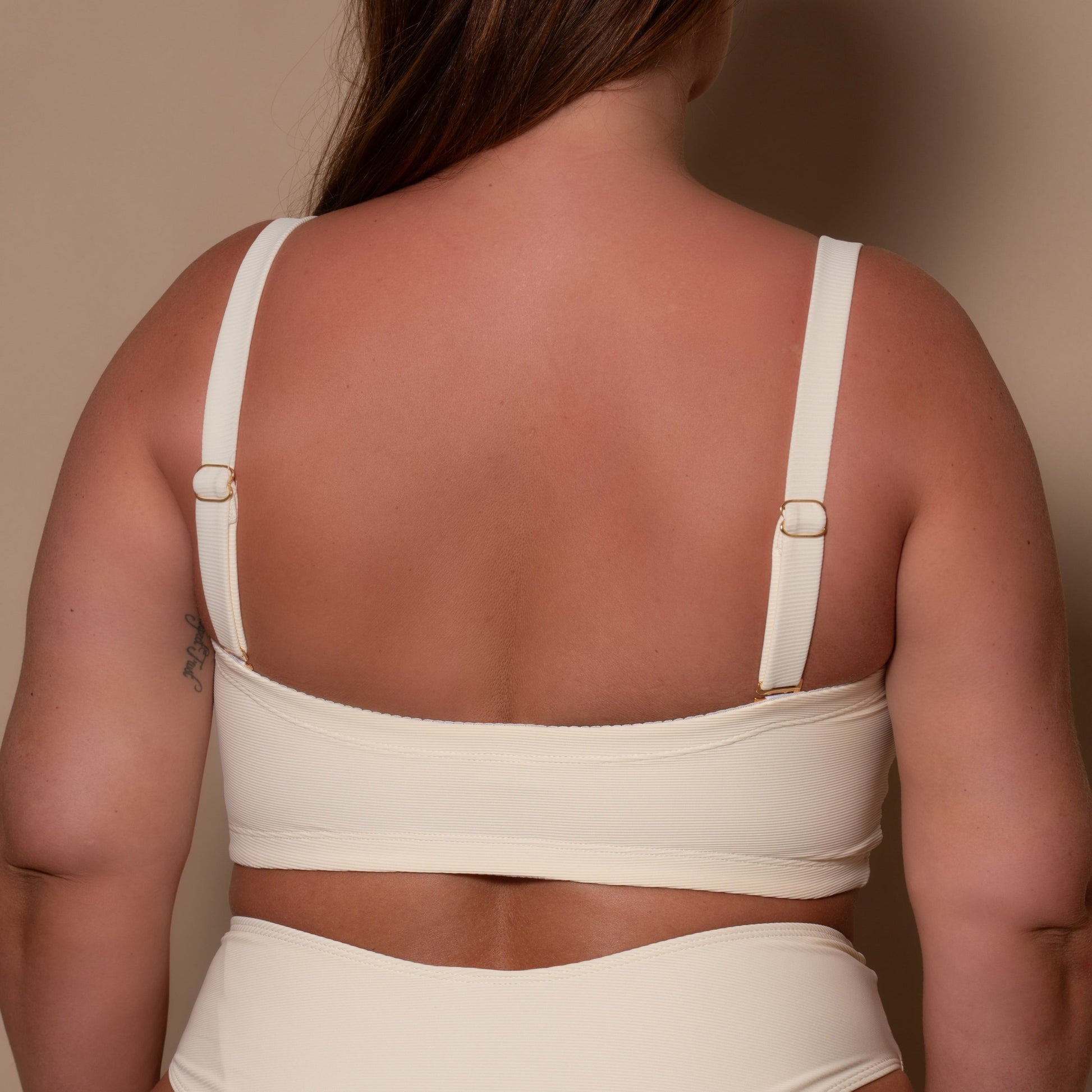 plussize woman wearing a cream white bikini  against a beige background