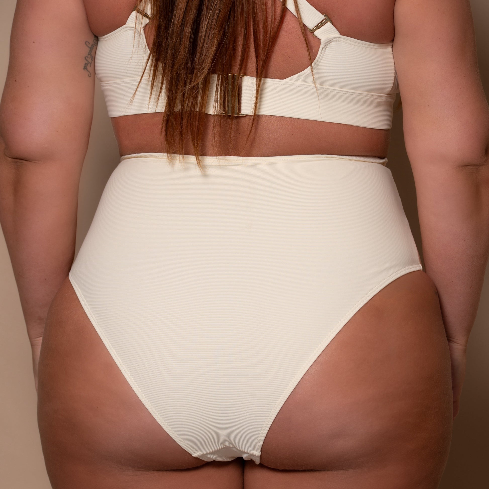 plussize woman wearing a cream white high waist bikini  against a beige background