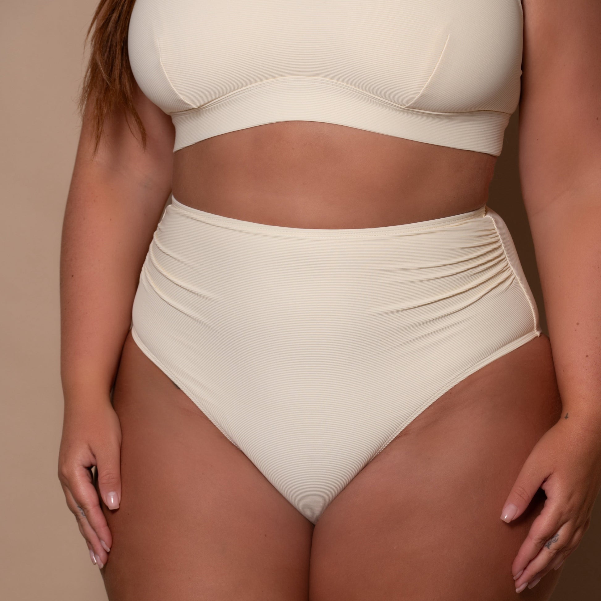 plussize woman wearing a cream white high waist bikini  against a beige background