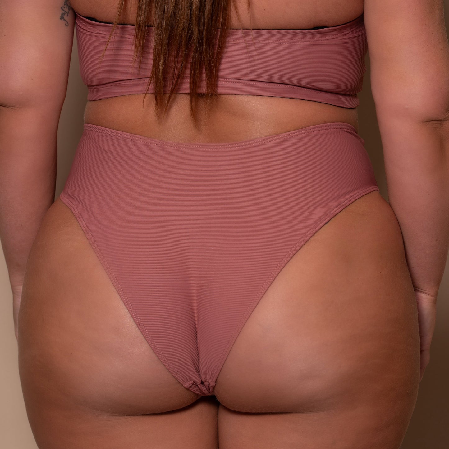 plussize woman wearing a rosewood pink briefs bikini  against a beige background