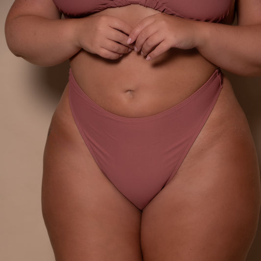plussize woman wearing a rosewood pink thong bikini  against a beige background