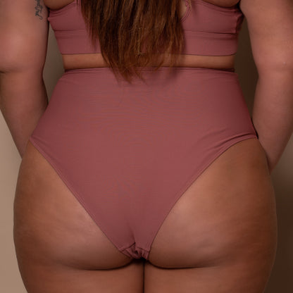 plussize woman wearing a rosewood pink high waist bikini  against a beige background