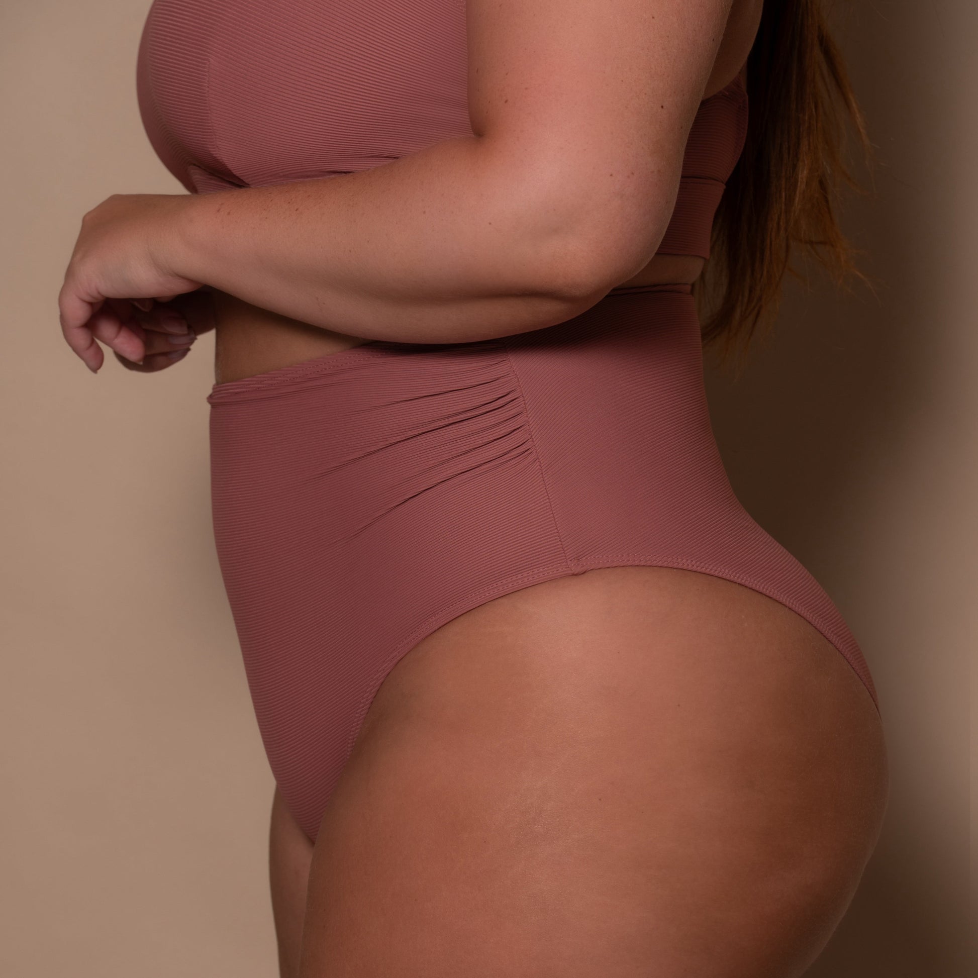 plussize woman wearing a rosewood pink high waist bikini  against a beige background