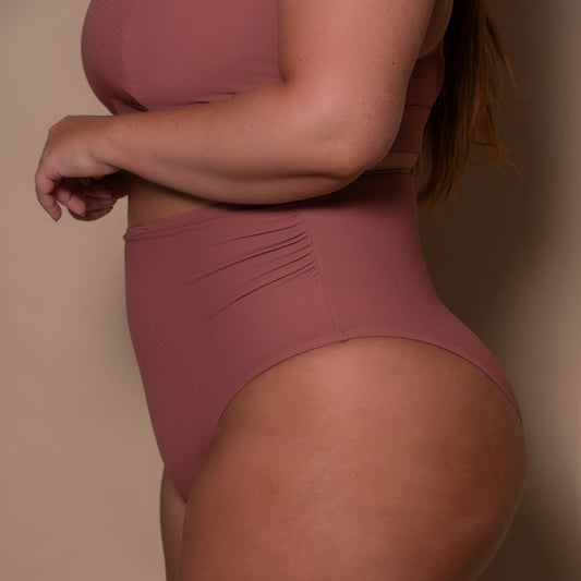 plussize woman wearing a rosewood pink high waist bikini  against a beige background