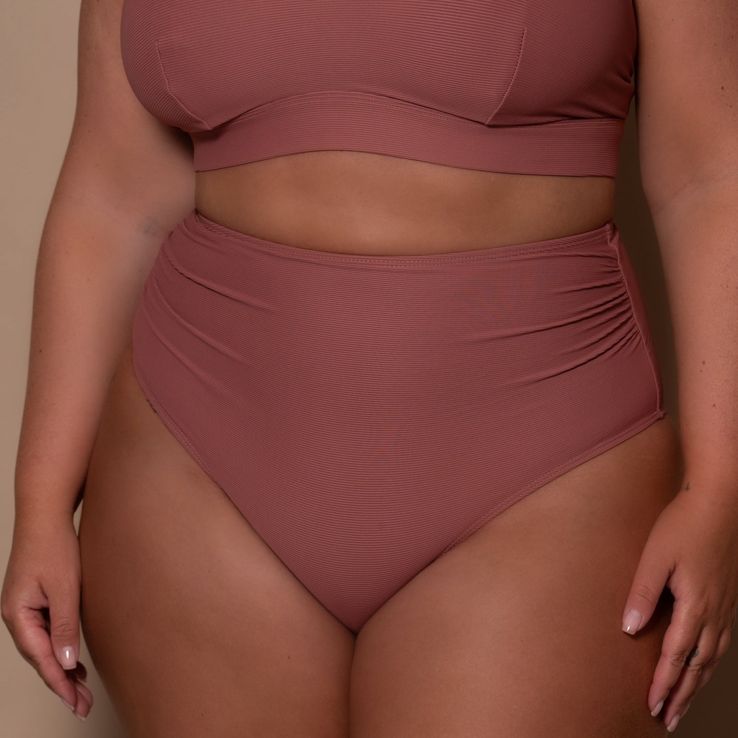 plussize woman wearing a rosewood pink high waist bikini  against a beige background